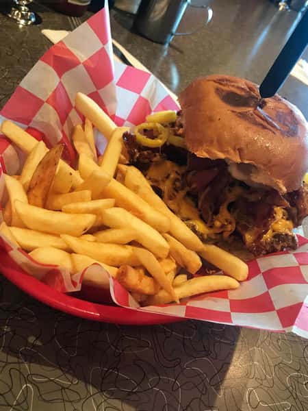 a bacon cheeseburger on a basket with a side of fries