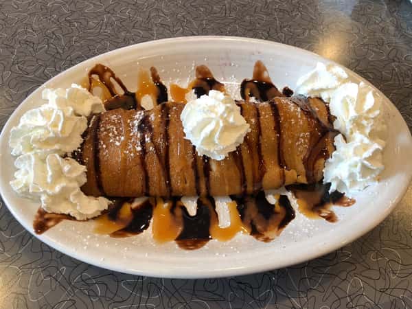 a breakfast crepe covered in whipped cream, and drizzled with chocolate syrup and caramel