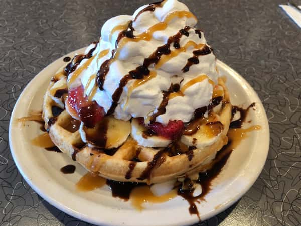 a belgian waffle on a plate with whipped cream, strawberries and chocolate drizzle
