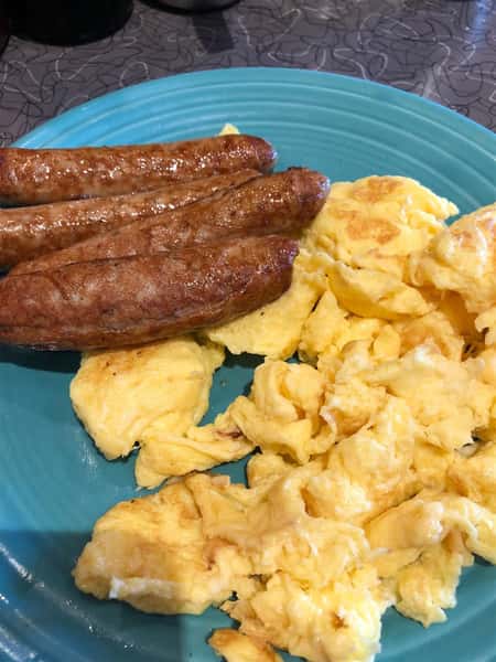 a blue plate with scrambled eggs and three breakfast sausages on it