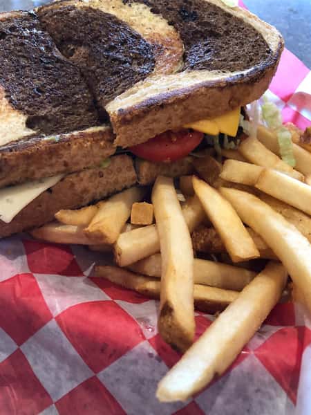 a cheeseburger with lettuce and tomato on marble rye with a side of fries
