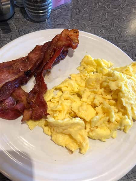 a plate of scrambled eggs and three pieces of bacon