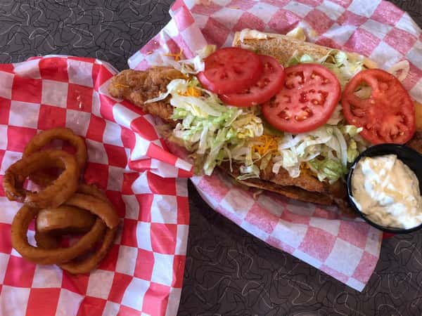 open faced chicken sandwich with cheese, lettuce, tomato and a side of dipping sauce with a side of onion rings