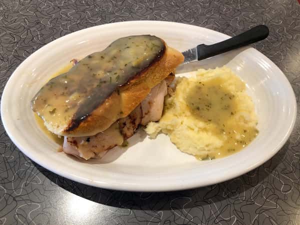 a turkey sandwich with a side of mashed potatoes both covered in gravy