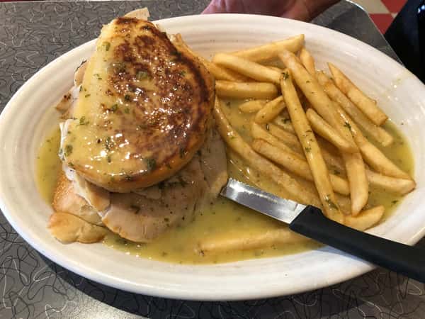 chicken sandwich on a plate with a side of fries covered in gravy