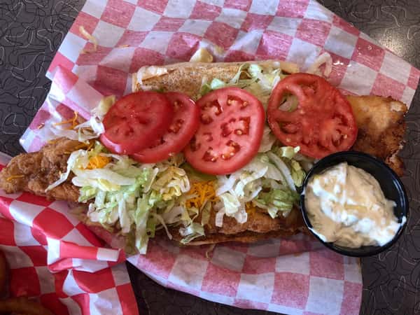 an open faced chicken sandwich with tomatoes, cheese, and lettuce and a side of dipping sauce in a basket