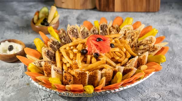 Shawarma platter with fries, sliced tomato, olives, pickled carrots, and peppers.