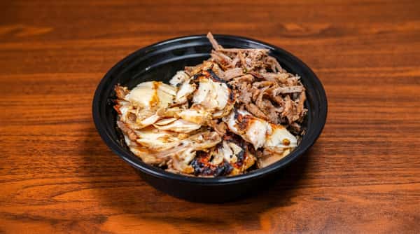 Black bowl with grilled chicken and shredded meat on a wooden table.