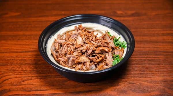 Shredded gyro meat served over hummus in a black bowl on a wooden table.