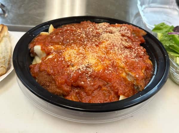 Breaded chicken cutlets topped with marinara sauce, melted cheese, and grated Parmesan in a black takeout container.