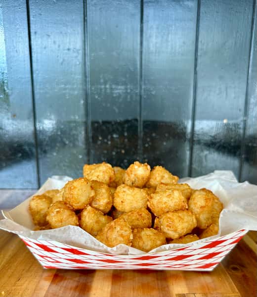 Golden crispy tater tots piled in a red and white checkered paper tray lined with parchment paper.