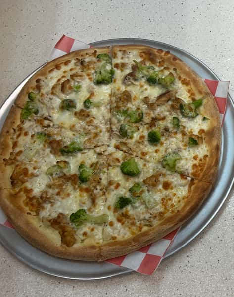 Whole white pizza topped with grilled chicken and broccoli on a silver tray lined with red and white paper.