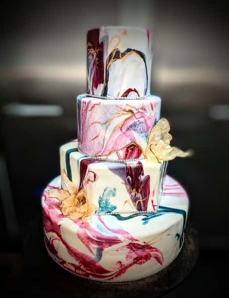 Four-tier marble effect cake with pink, burgundy, and teal swirls, decorated with gold butterflies and metallic accents.