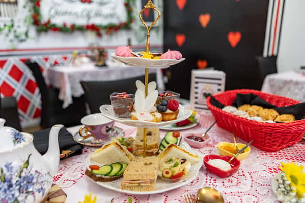 Three-tiered afternoon tea stand with assorted finger sandwiches, bunny-themed sweets, chocolate mousse, and meringues in a Queen of Hearts tea room.
