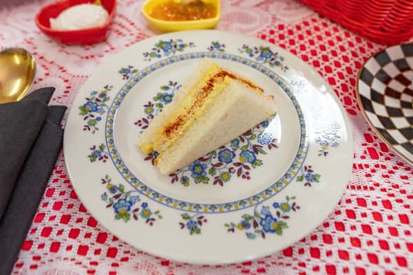 Creamy egg salad sandwich on soft white bread, lightly dusted with paprika, served on a vintage floral plate.