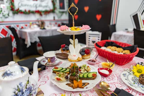 Three-tiered afternoon tea stand with assorted finger sandwiches, bunny-themed sweets, chocolate mousse, and meringues in a Queen of Hearts tea room.