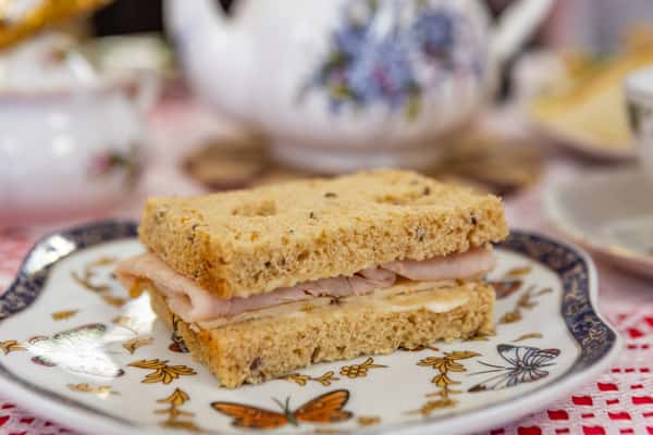 Delicate tea sandwich with sliced turkey and cheese on multigrain bread, served on a butterfly-themed porcelain plate.