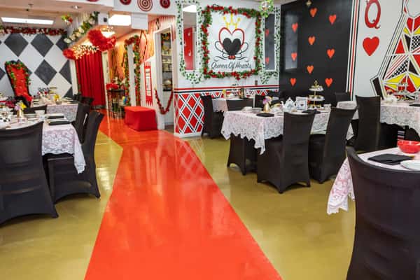 Whimsical Queen of Hearts-themed tea room with red and black card suit decor, lace-covered tables, and vibrant Alice in Wonderland flair.