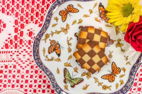Checkerboard shortbread cookies with vanilla and chocolate squares, served on a butterfly-themed plate with floral garnish.