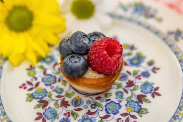 Mini fruit tart topped with fresh blueberries and a raspberry, dusted with edible gold, served on a floral vintage dessert plate.