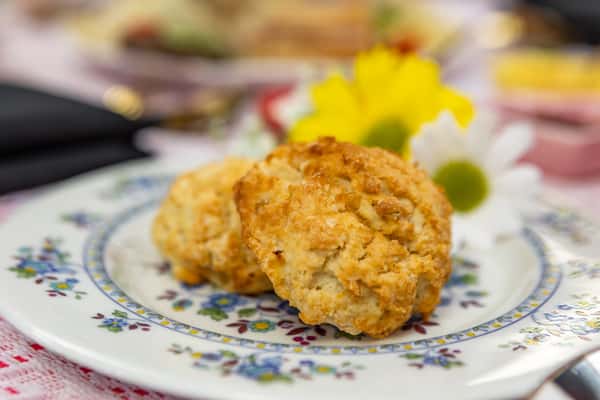 Golden brown tea scones with a crisp exterior, served on a floral china plate with daisy and yellow flower accents.