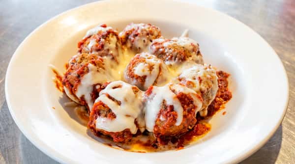 Meatballs covered in red sauce and melted white cheese on a white plate.