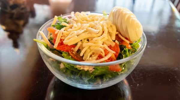 Green salad with lettuce, tomato, shredded cheese, and a sliced hard-boiled egg in a clear bowl.