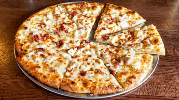 Pizza with melted white cheese, diced chicken, and bacon pieces on a metal pan.