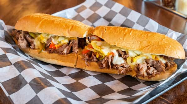 Philly cheesesteak sandwich with shaved beef, melted white cheese, onions, peppers, and pickles on a hoagie roll.