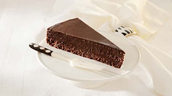 Dark chocolate cake slice with glossy ganache topping on a white plate with a fork.