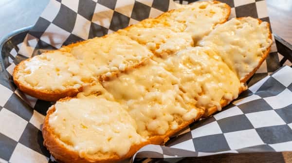Cheesy garlic bread with melted mozzarella served in a basket lined with black and white checkered paper.