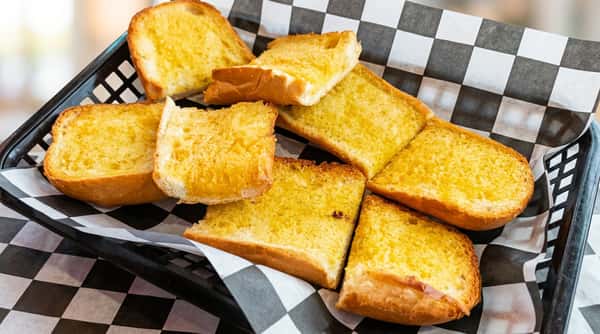 Golden garlic bread slices, some toasted, arranged in a basket lined with black and white checkered paper.