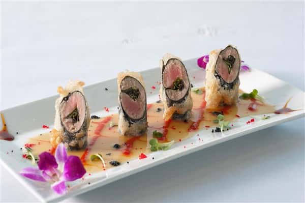 Sushi platter with 4 different rolls and sauce layered along the bottom of the platter