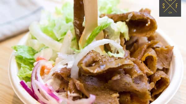 Doner kebab meat served with fresh lettuce, onion and tomato in a takeaway container.