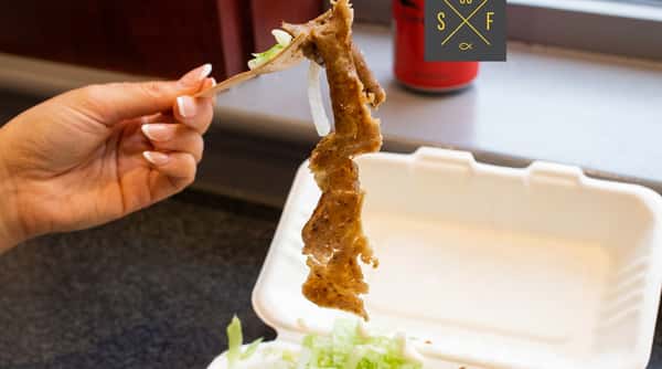 Doner meat being served into a takeaway box with fresh salad on the side.