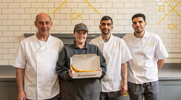 Sixty Fish team members standing together inside the Coleshill shop with a freshly prepared takeaway order.