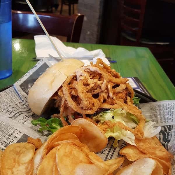 Crispy onion ring-topped sandwich with lettuce on a bun, served with golden house-made potato chips.
