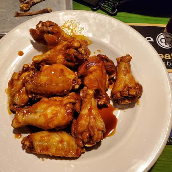 Plate of saucy buffalo chicken wings arranged on a white dish.