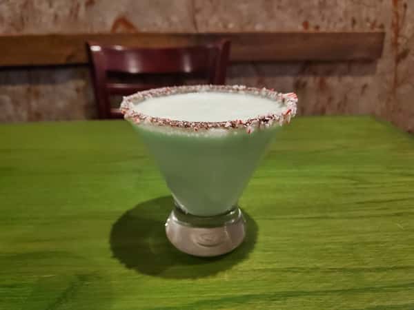 Minty holiday cocktail with a light blue hue, served in a glass rimmed with crushed peppermint candy.