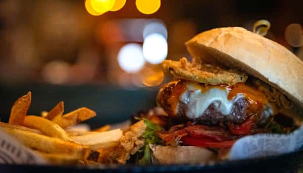 Juicy cheeseburger with crispy onion rings, bacon, and fries served in a dimly lit restaurant setting.