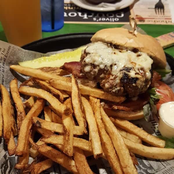 Cheeseburger topped with bacon and blue cheese, served with crispy fries, a pickle spear, and dipping sauce.