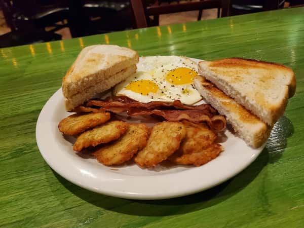 Classic breakfast plate with sunny-side-up eggs, crispy bacon, hash brown patties, and toasted white bread.