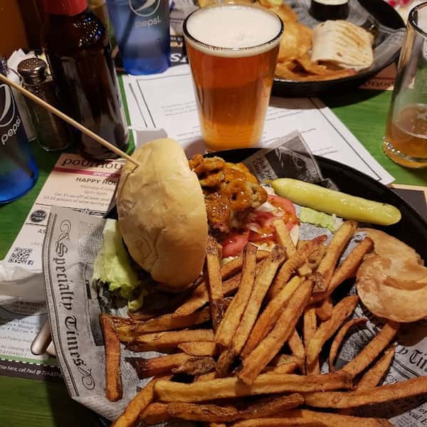 Burger with lettuce, tomato, fried jalapeños, and fries, served with a pickle spear and pint of beer on a newspaper-lined tray.