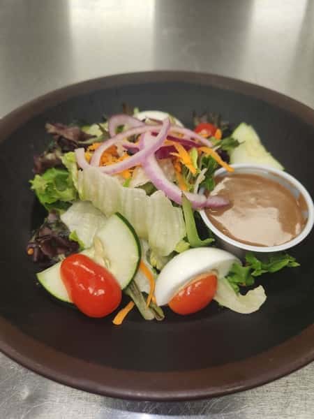 Fresh garden salad with grape tomatoes, cucumber slices, egg wedges, and red onion served with a side of creamy dressing.