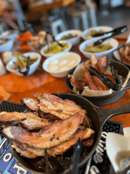 J.D.'s Bar-B-Que buffet featuring thick-cut smoked pork belly and bacon in cast iron skillets alongside pickled eggs and relish.