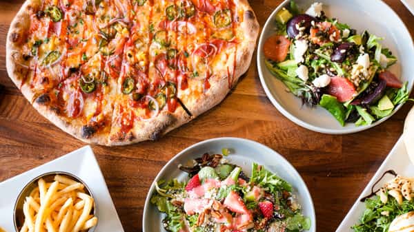 Wood-fired artisan pizza served with fresh seasonal salads and crispy fries, showcasing a vibrant casual dining spread perfect for sharing.