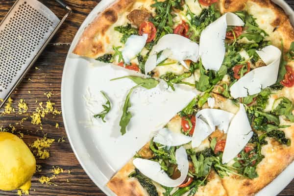 Gourmet artisan pizza topped with arugula, cherry tomatoes, shaved parmesan and fresh herbs on a crispy wood-fired crust.