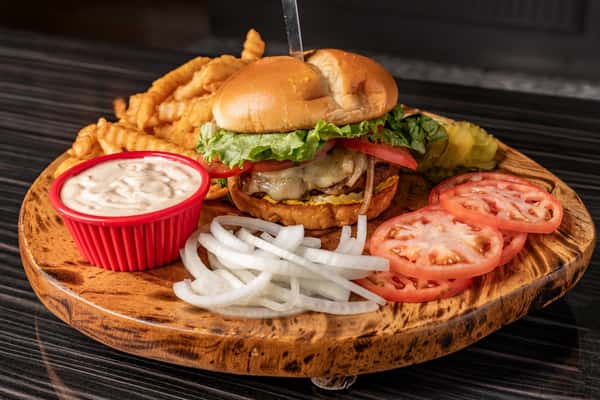 wooden board withgrilled chicken sandwich, onions, tomatoes, fries, and dipping sauce