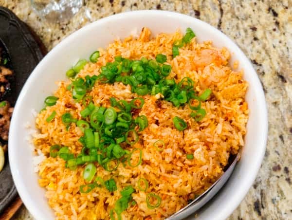 A bowl of shrimp fried rice mixed with eggs and vegetables, topped with freshly chopped green onions for a flavorful and satisfying dish.