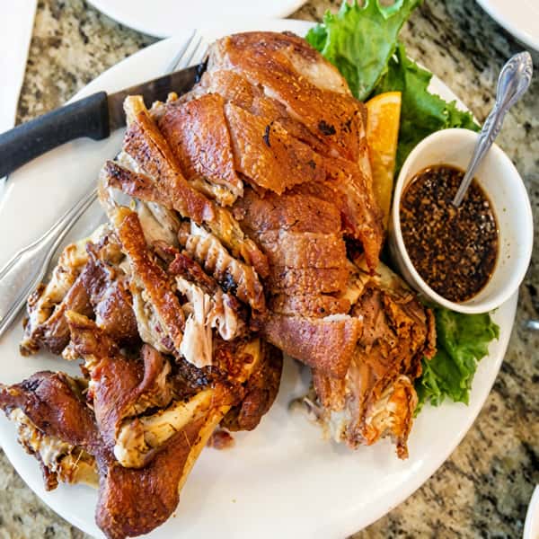 Crispy pork hock with golden crackling skin, served with fresh vegetables and a savory dipping sauce.